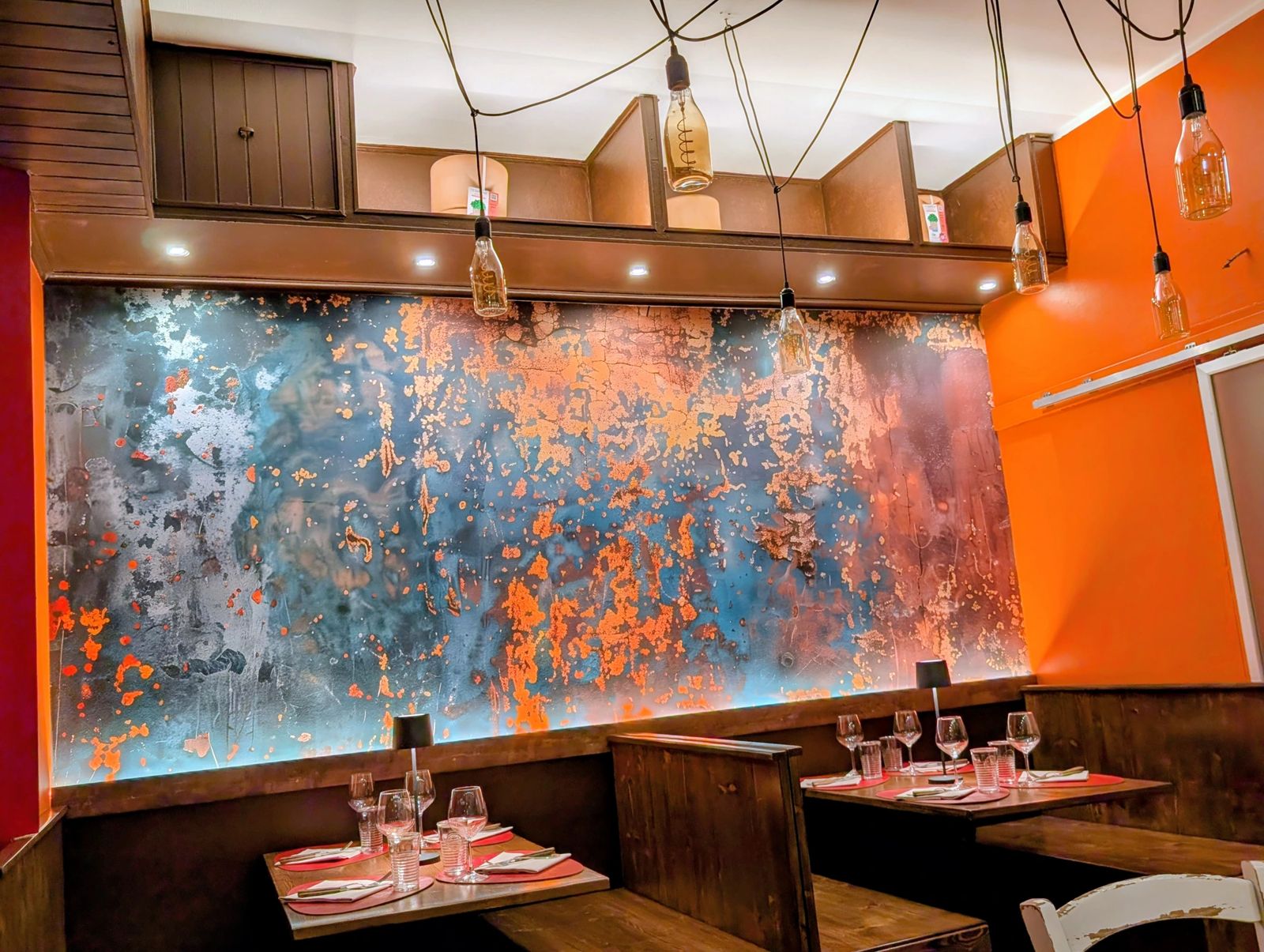 Blue and copper oxidised wall with pendant lamps and wooden tables